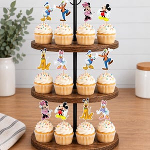 May include: A three-tiered wooden cupcake stand holding twelve cupcakes topped with colorful sprinkles and paper character toppers featuring Mickey Mouse, Minnie Mouse, Donald Duck, Daisy Duck, Goofy, and Pluto on thin wooden picks.