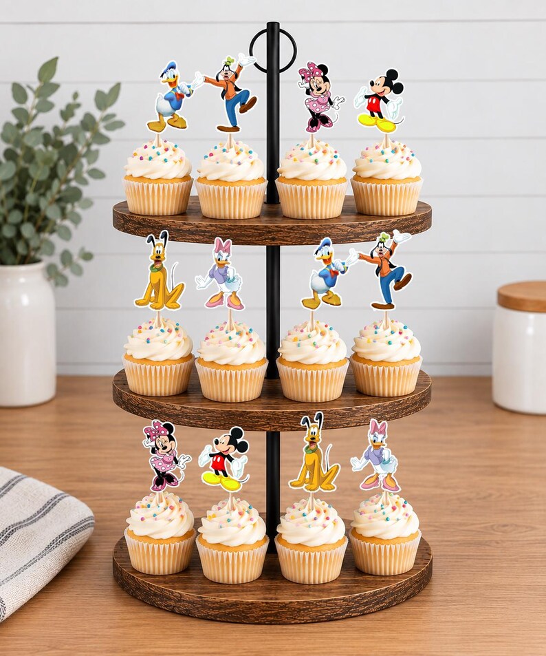 May include: A three-tiered wooden cupcake stand holding twelve cupcakes topped with colorful sprinkles and paper character toppers featuring Mickey Mouse, Minnie Mouse, Donald Duck, Daisy Duck, Goofy, and Pluto on thin wooden picks.