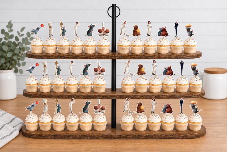 May include: A three-tiered wooden cupcake stand holding thirty-six cupcakes, each topped with a small paper cutout of a character from the movie Ratatouille. The cupcakes feature white frosting with colorful sprinkles and are arranged in three rows.
