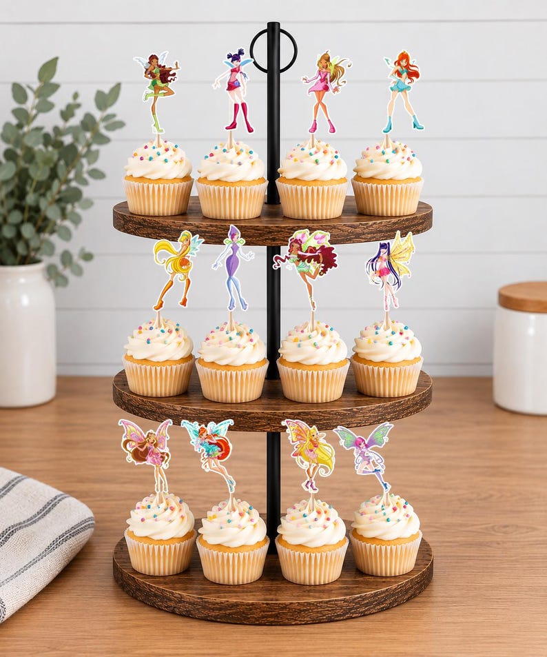 May include: A three-tiered wooden cupcake stand holding twelve cupcakes, each topped with a white frosting swirl, colorful sprinkles, and a decorative paper cutout of a Winx Club fairy character attached to a thin wooden pick.