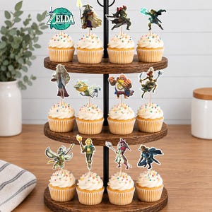 May include: A three-tiered wooden cupcake stand holding twelve cupcakes topped with white frosting and colourful sprinkles. Each cupcake features a decorative paper topper depicting various characters and the logo from The Legend of Zelda: Tears of the Kingdom.