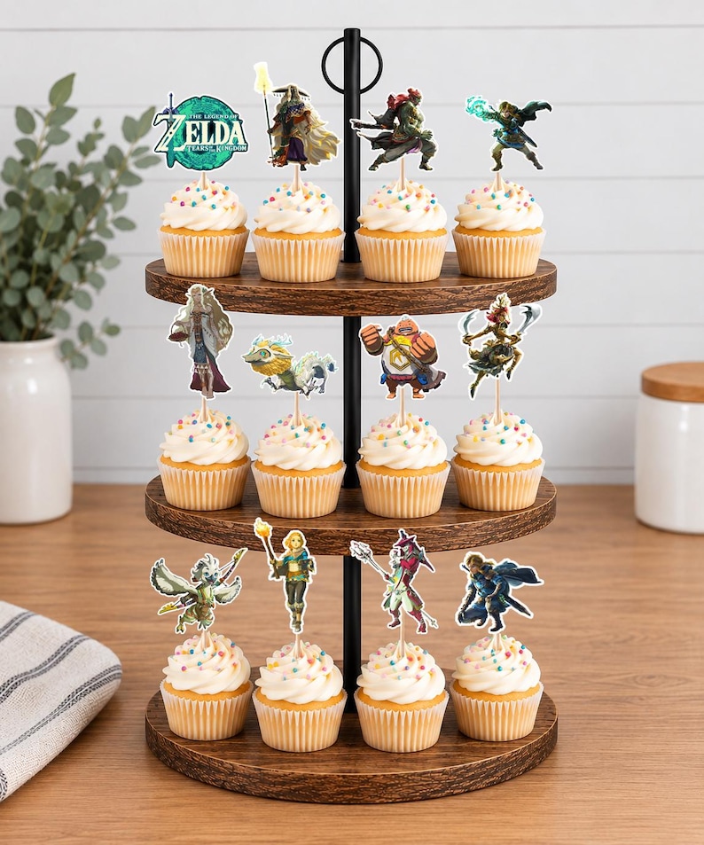 May include: A three-tiered wooden cupcake stand holding twelve cupcakes topped with white frosting and colourful sprinkles. Each cupcake features a decorative paper topper depicting various characters and the logo from The Legend of Zelda: Tears of the Kingdom.