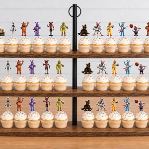 May include: A three-tiered wooden cupcake stand holding numerous cupcakes topped with various Five Nights at Freddy's character paper toppers. The toppers feature colourful illustrations of animatronic figures, including bears, rabbits, and foxes, arranged in rows across the three tiers.