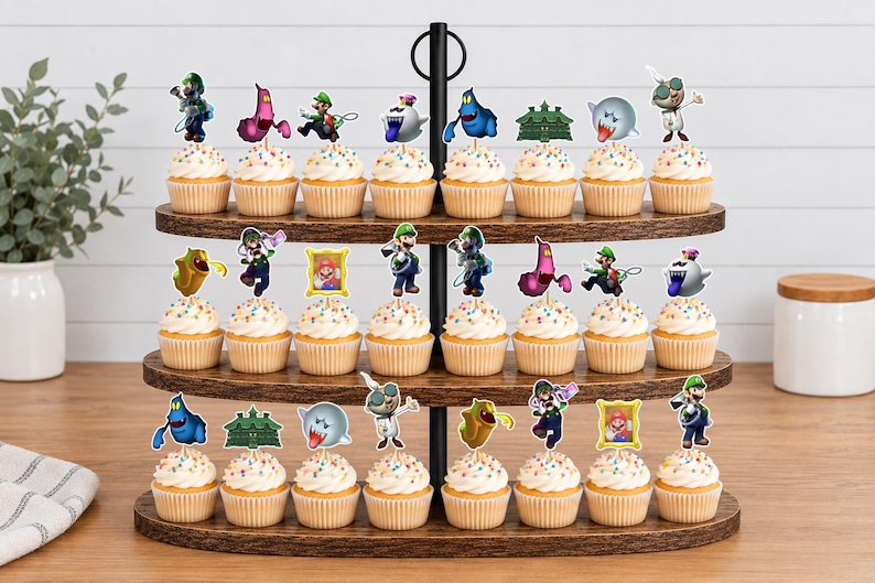 May include: A three-tiered wooden cupcake stand holding twenty-four cupcakes, each topped with a colorful paper cutout featuring characters and icons from the Luigi's Mansion video game series, including Luigi, ghosts, and framed portraits.