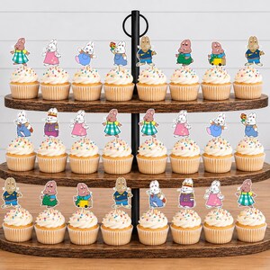 May include: A three-tiered dark wood cupcake stand holding twenty-four cupcakes, each topped with a colorful paper cutout of a cartoon rabbit character. The stand features a central black metal handle and oval-shaped shelves with a wood grain finish.