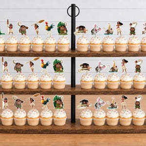 Op de afbeelding: Een houten cupcake-standaard met drie niveaus vol cupcakes met papieren decoraties in Moana-thema. De prikkers tonen diverse personages waaronder Moana, Maui, het varkentje Pua, de haan Heihei en andere iconen uit de bekende animatiefilm.