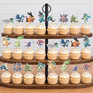 K&ouml;nnte beinhalten: Ein dreist&ouml;ckiger Cupcake-St&auml;nder aus dunklem Holz mit vierundzwanzig Cupcakes, die mit bunten Streuseln und verschiedenen Pok&eacute;mon-Papieraufsteckern, einschlie&szlig;lich des Pok&eacute;mon Legends-Logos, auf drei ovalen Holzablagen dekoriert sind.