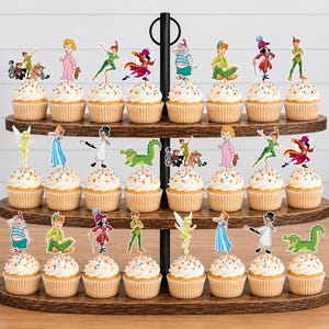 May include: A three-tiered wooden cupcake stand holding twenty-four cupcakes, each topped with a colorful paper cutout of Peter Pan characters including Peter Pan, Tinker Bell, Captain Hook, Wendy, and a green crocodile, featuring rainbow sprinkles.