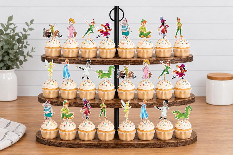May include: A three-tiered wooden cupcake stand holding twenty-four cupcakes, each topped with a colorful paper cutout of Peter Pan characters including Peter Pan, Tinker Bell, Captain Hook, Wendy, and a green crocodile, featuring rainbow sprinkles.