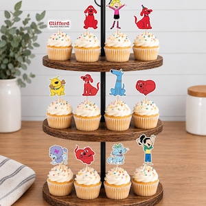 Pode incluir: Um suporte de madeira de tr&ecirc;s n&iacute;veis para cupcakes com doze bolinhos cobertos com glac&ecirc; branco e granulado colorido. Cada cupcake possui um topo de papel com personagens de Clifford, o c&atilde;o vermelho, incluindo Clifford e seus amigos animais.