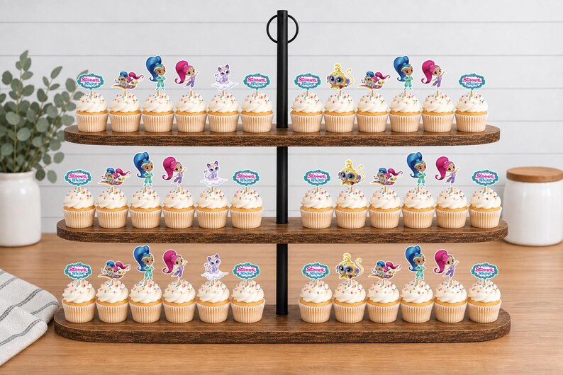 May include: A three-tiered wooden cupcake stand holding numerous cupcakes topped with Shimmer and Shine character paper toppers. Each topper features colorful cartoon figures or the Shimmer and Shine logo. The cupcakes have white frosting.