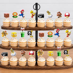 May include: A three-tiered wooden cupcake stand holding twenty-four cupcakes, each topped with a decorative paper cutout featuring various Super Mario characters and game icons like bricks, mushrooms, flowers, and question blocks.