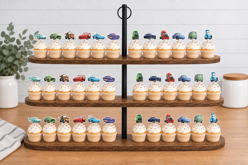 May include: A three-tiered wooden cupcake stand holding numerous cupcakes topped with colorful paper cutouts of various cartoon cars. Each cupcake features white frosting and a unique character topper, arranged in rows on the dark brown wooden shelves.