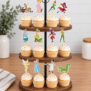 May include: A three-tiered wooden cupcake stand holding twelve cupcakes topped with white frosting and colorful sprinkles. Each cupcake features a decorative paper topper depicting various Peter Pan characters, including Peter Pan, Wendy, Tinker Bell, and Captain Hook.