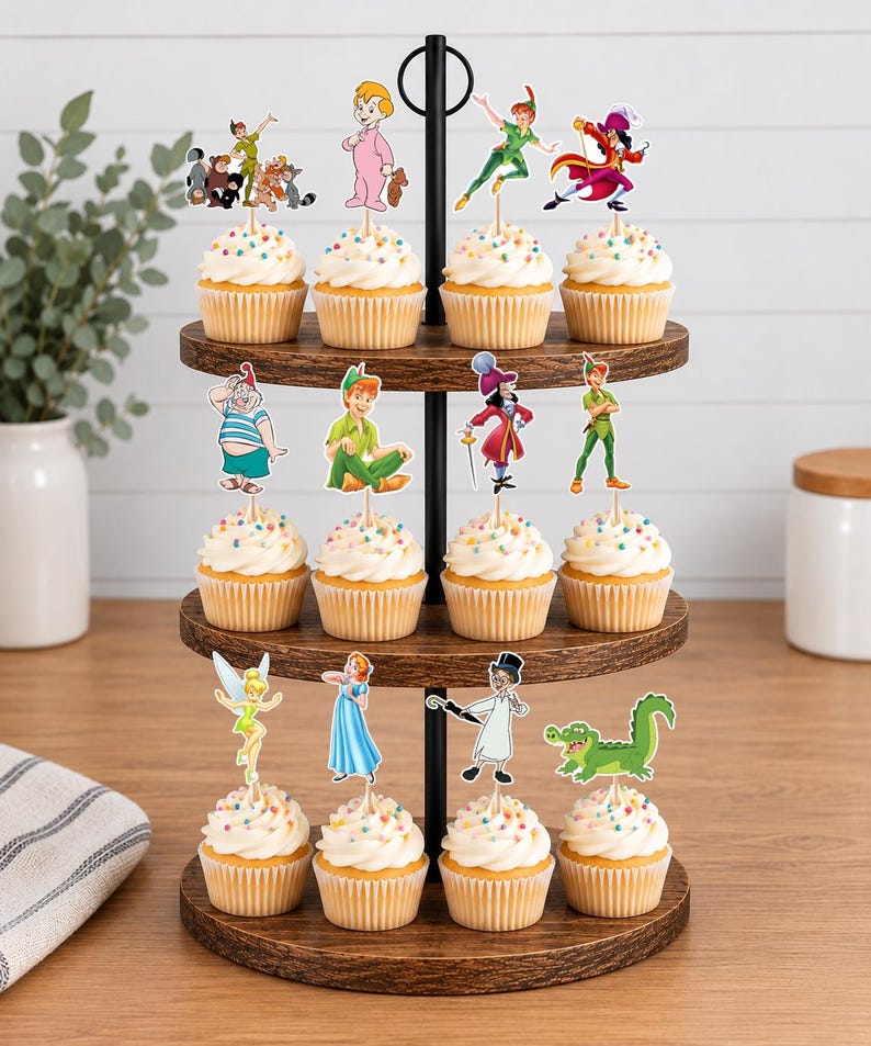 May include: A three-tiered wooden cupcake stand holding twelve cupcakes topped with white frosting and colorful sprinkles. Each cupcake features a decorative paper topper depicting various Peter Pan characters, including Peter Pan, Wendy, Tinker Bell, and Captain Hook.