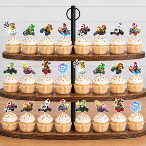 Op de afbeelding: Een houten cupcake-standaard met drie niveaus en vierentwintig cupcakes, elk voorzien van een decoratieve papieren uitsparing met verschillende Mario Kart-personages, voertuigen en spelpictogrammen.