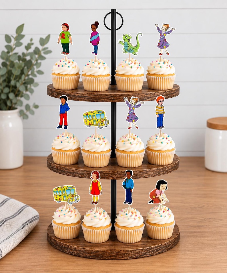 May include: A three-tiered wooden cupcake stand holding twelve cupcakes, each topped with a paper cutout of characters and a school bus from The Magic School Bus. The cupcakes feature white frosting with colorful sprinkles in paper liners.