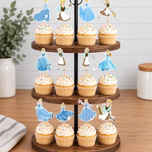 May include: A three-tiered wooden cupcake stand holding twelve cupcakes topped with white frosting and colorful sprinkles. Each cupcake features a paper cutout topper depicting a character in various blue dresses or brown and white work clothing.