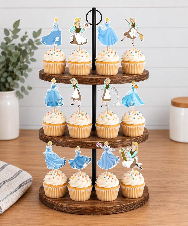 May include: A three-tiered wooden cupcake stand holding twelve cupcakes topped with white frosting and colorful sprinkles. Each cupcake features a paper cutout topper depicting a character in various blue dresses or brown and white work clothing.
