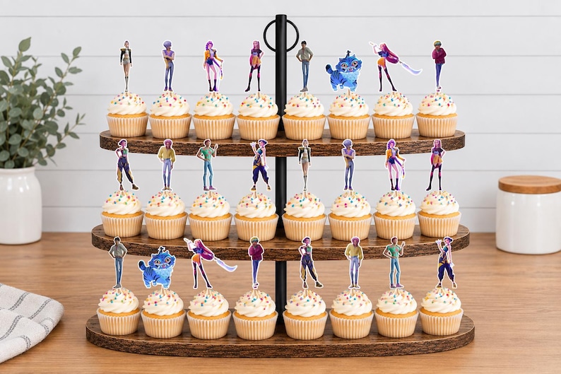Op de afbeelding: Een houten cupcake-standaard met drie niveaus en vierentwintig cupcakes, elk voorzien van een kleine, kleurrijke papieren uitsparing van diverse geanimeerde figuren, waaronder menselijke figuren en een blauw katachtig wezen.