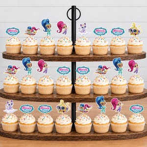 May include: A three-tiered wooden cupcake stand holding twenty-four cupcakes topped with colorful Shimmer and Shine character paper toppers. Each cupcake features a light-colored frosting with multi-colored sprinkles and a decorative paper cutout.