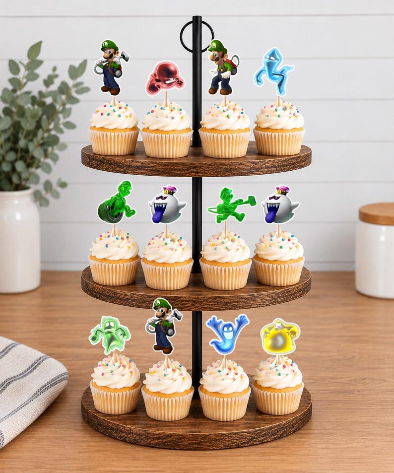 Puede incluir: Un soporte de madera para cupcakes de tres niveles con doce cupcakes cubiertos de glaseado blanco y chispas de colores. Cada cupcake tiene un adorno de papel decorativo que representa personajes de la serie de juegos Luigi's Mansion.