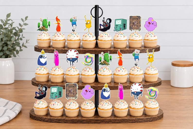 K&ouml;nnte beinhalten: Ein dreist&ouml;ckiger Cupcake-St&auml;nder aus Holz mit vierundzwanzig Cupcakes, die mit bunten Papieraufsteckern verziert sind, welche verschiedene Adventure Time-Figuren wie Finn, Jake, Prinzessin Bubblegum und den Eisk&ouml;nig zeigen.