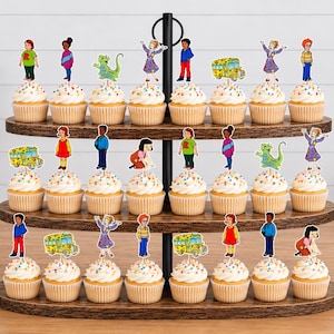 May include: A three-tiered wooden cupcake stand holding twenty-four cupcakes, each topped with a colorful paper cutout featuring characters and a yellow school bus from the Magic School Bus series, arranged in rows on the dark brown wooden shelves.