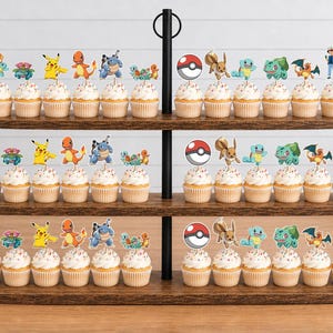 May include: A three-tiered wooden cupcake stand holding numerous cupcakes topped with colorful paper cutouts of various Pokemon characters, including Pikachu, Charmander, Squirtle, Bulbasaur, Eevee, and Poke Balls, arranged in uniform rows.
