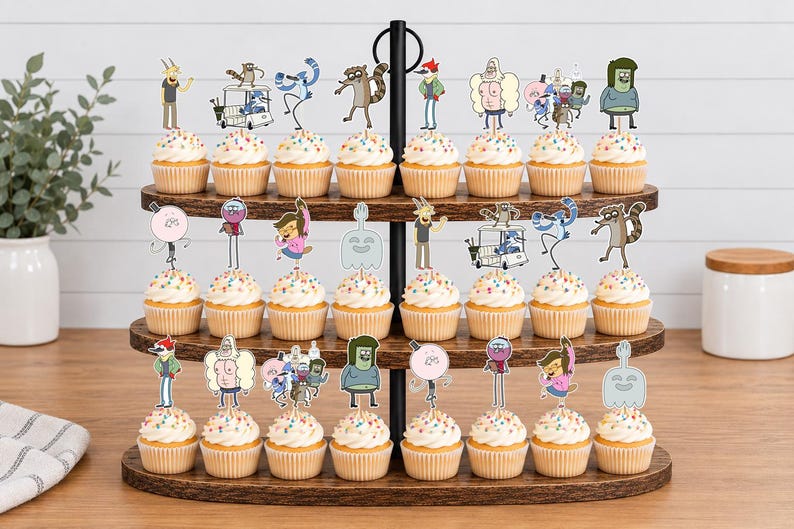 K&ouml;nnte beinhalten: Ein dreist&ouml;ckiger Cupcake-St&auml;nder aus Holz mit vierundzwanzig Cupcakes, die jeweils mit einem Papieraufsteller von Charakteren aus der Zeichentrickserie Regular Show verziert sind, darunter Mordecai, Rigby, Benson, Skips, Pops, Muscle Man und High Five Ghost.