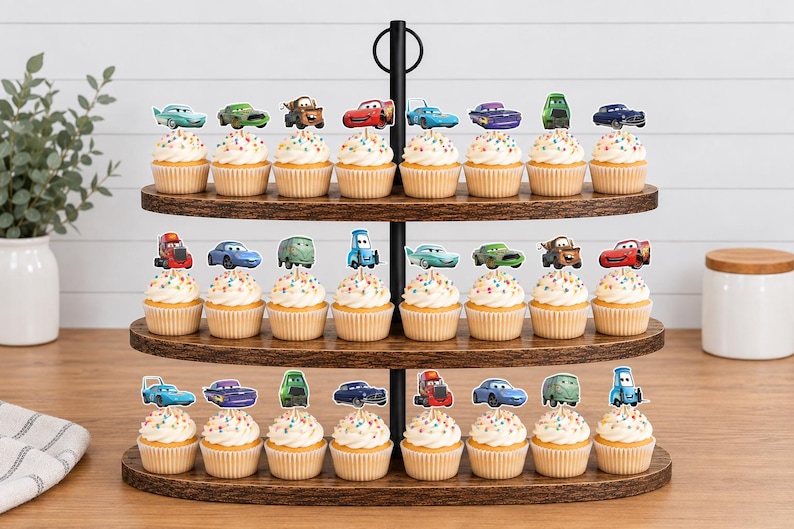 May include: A three-tiered wooden cupcake stand holding twenty-three cupcakes, each topped with a colorful paper cutout of a character from the Cars movie franchise, featuring various vehicle designs in red, blue, green, and purple hues.