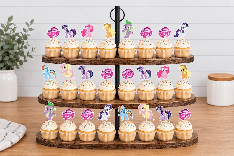Op de afbeelding: Een houten cupcake-standaard met drie niveaus met vierentwintig cupcakes, versierd met kleurrijke My Little Pony-papieren toppers en My Little Pony-logo's. De standaard heeft een zwarte metalen handgreep in het midden en ovale houten lagen.