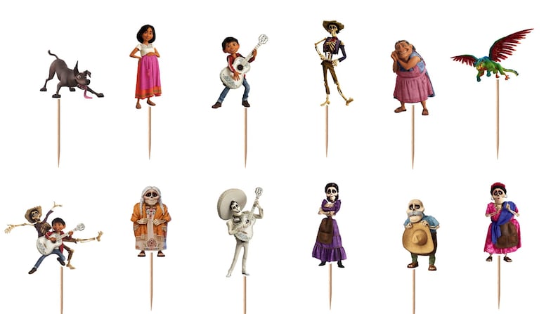 May include: A set of twelve decorative cupcake toppers featuring various animated characters from the movie Coco, including a dog, a boy with a guitar, skeletons in colourful clothing, and a winged creature, each attached to a thin wooden pick.