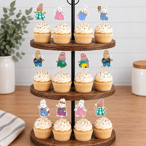 May include: A three-tiered wooden cupcake stand holding twelve cupcakes, each topped with a white frosting swirl, colorful sprinkles, and a paper cutout of a cartoon rabbit character in various outfits and poses, arranged in four rows of three.