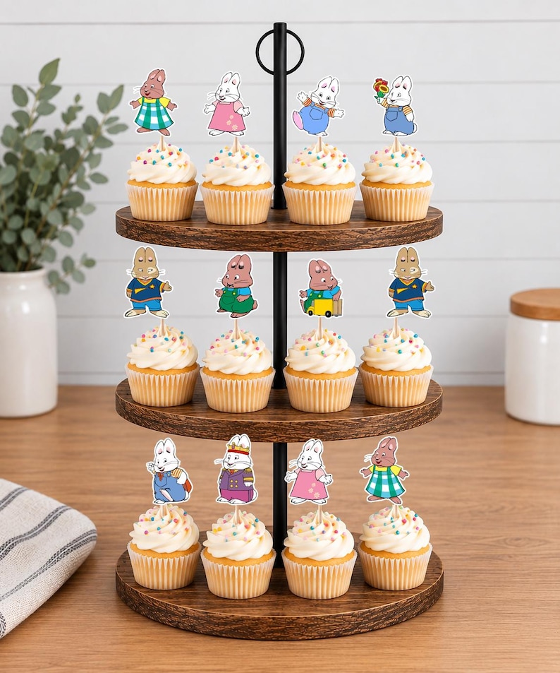 May include: A three-tiered wooden cupcake stand holding twelve cupcakes, each topped with a white frosting swirl, colorful sprinkles, and a paper cutout of a cartoon rabbit character in various outfits and poses, arranged in four rows of three.