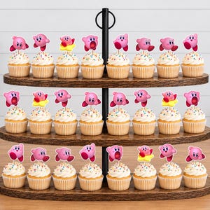 May include: A three-tiered dark wood cupcake stand holding twenty-four cupcakes, each topped with a paper cutout of the pink character Kirby in various poses. The cupcakes feature white frosting with colorful sprinkles in light brown paper liners.