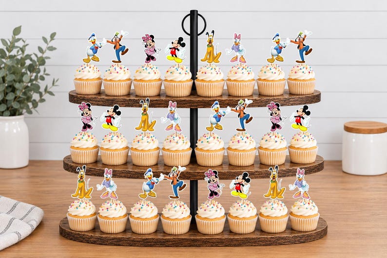 May include: A three-tiered wooden cupcake stand holding twenty-four cupcakes topped with colorful sprinkles and paper cutouts of various cartoon characters including Mickey Mouse, Minnie Mouse, Donald Duck, Daisy Duck, Goofy, and Pluto.