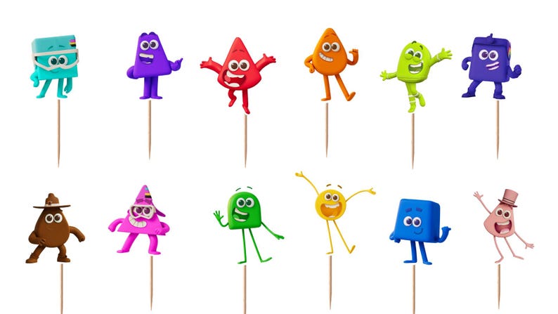 May include: A set of twelve colorful cupcake toppers featuring various cartoon characters with distinct shapes, expressions, and accessories, each attached to a thin wooden pick. The characters include a blue square, purple triangle, red triangle, orange teardrop, lime green blob, dark purple square, brown blob with a hat, pink triangle with goggles, green square, yellow circle, blue square, and a light pink blob with a top hat.