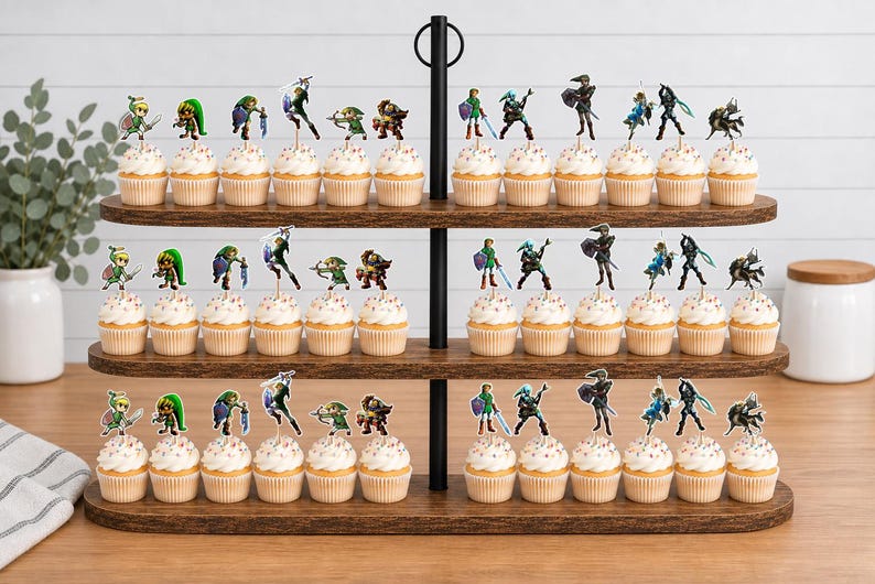 Op de afbeelding: Een houten cupcake-standaard met drie niveaus met talloze cupcakes, elk bekroond met kleine, kleurrijke papieren uitsparingen van diverse videogamepersonages in actiehoudingen, waaronder figuren met zwaarden, schilden en bogen op elke plank.