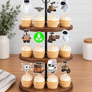 May include: A three-tiered wooden cupcake stand holding twelve cupcakes topped with white frosting and colorful sprinkles. Each cupcake features a paper topper depicting characters and icons from the movie Wall-E, including robots, a spaceship, and a green leaf symbol.