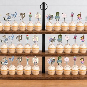 K&ouml;nnte beinhalten: Ein dreist&ouml;ckiger Cupcake-St&auml;nder aus Holz mit zahlreichen Cupcakes, die mit Papieraufstellern verschiedener Zeichentrickfiguren aus der Serie Regular Show verziert sind, darunter Mordecai, Rigby, Benson, Skips, Pops, Muscle Man und High Five Ghost.