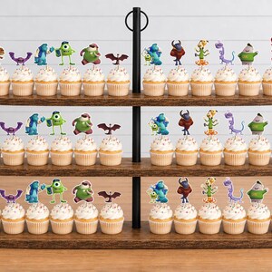 May include: A three-tiered wooden cupcake stand holding numerous cupcakes topped with colorful character toppers. The toppers feature various animated creatures, including a green one-eyed character, a blue furry figure, and others, arranged in rows.