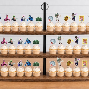 May include: A three-tiered wooden cupcake stand holding rows of cupcakes topped with various character-themed paper toppers. The toppers feature colorful illustrations of ghosts, Luigi, and other figures from the Luigi's Mansion video game series.