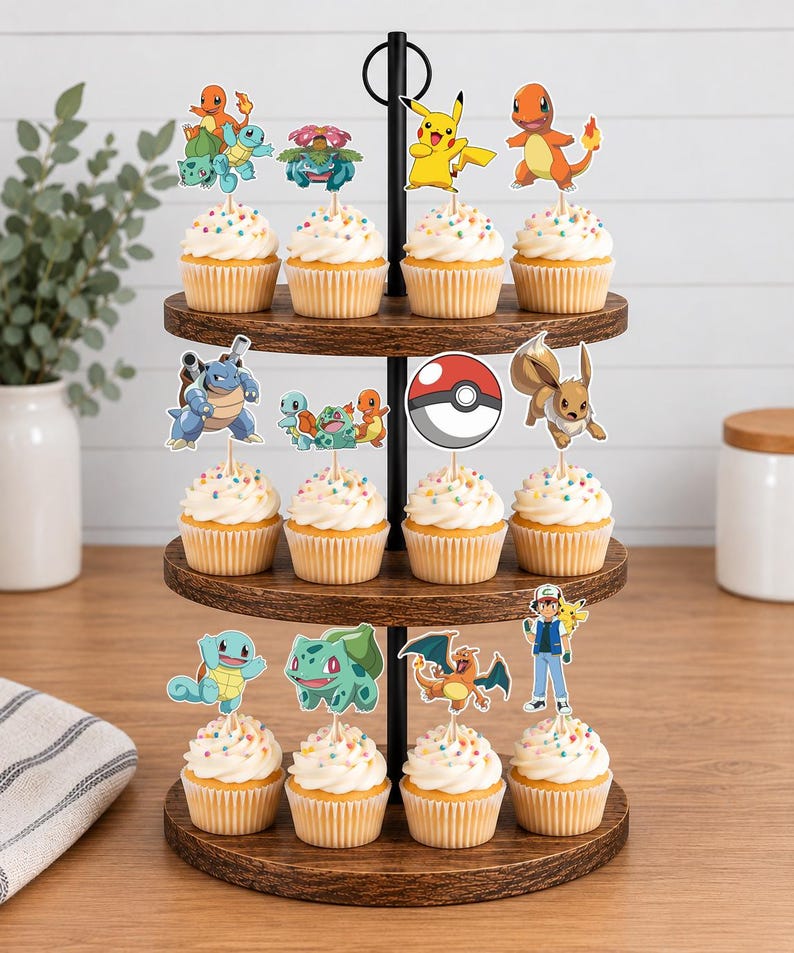 May include: A three-tiered wooden cupcake stand holding twelve cupcakes, each topped with a colorful paper cutout of various Pokemon characters, including Pikachu, Charmander, Squirtle, Bulbasaur, Eevee, Blastoise, Charizard, and a trainer figure.