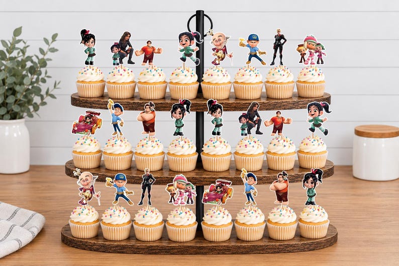 May include: A three-tiered wooden cupcake stand holding twenty-four cupcakes, each topped with a colorful paper cutout featuring characters from the Wreck-It Ralph movie franchise, including Ralph, Vanellope, and Felix, with rainbow sprinkles.