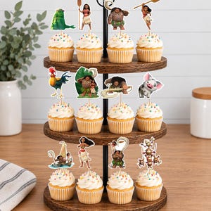 Op de afbeelding: Een houten cupcake-standaard met drie niveaus en twaalf cupcakes, afgewerkt met witte glazuur en kleurrijke hagelslag. Elke cupcake is voorzien van een decoratieve papieren topper met personages uit de animatiefilm Moana.