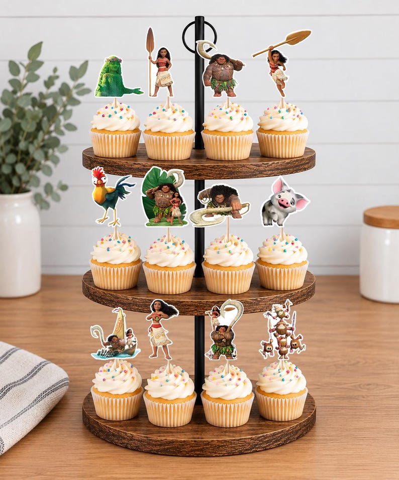 Op de afbeelding: Een houten cupcake-standaard met drie niveaus en twaalf cupcakes, afgewerkt met witte glazuur en kleurrijke hagelslag. Elke cupcake is voorzien van een decoratieve papieren topper met personages uit de animatiefilm Moana.