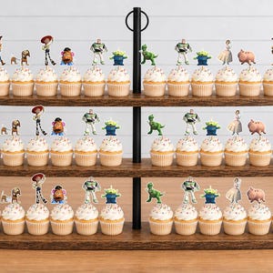 May include: A three-tiered wooden cupcake stand holding numerous cupcakes topped with small, colourful paper cutouts of various animated characters, including a cowboy, a space ranger, a green alien, a dinosaur, a pig, and a potato-shaped figure.