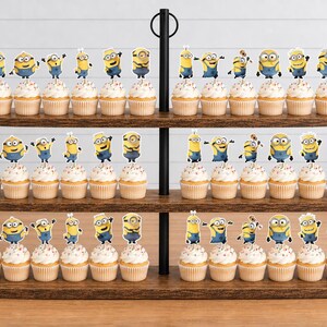 May include: A three-tiered wooden cupcake stand holding numerous cupcakes topped with yellow Minion character paper toppers. Each cupcake features a light-colored frosting with colorful sprinkles, arranged neatly across the three oval wooden shelves.