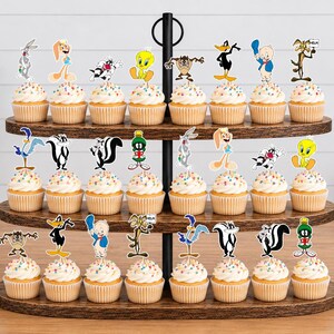 以下が含まれることがあります： 3段の木製カップケーキスタンドに22個のカップケーキが並んでおり、それぞれにルーニー・テューンズのキャラクターのカラフルな紙製切り抜きが飾られています。キャラクターにはバッグス・バニー、トゥイーティー、ダフィー・ダック、タズなどが含まれています。